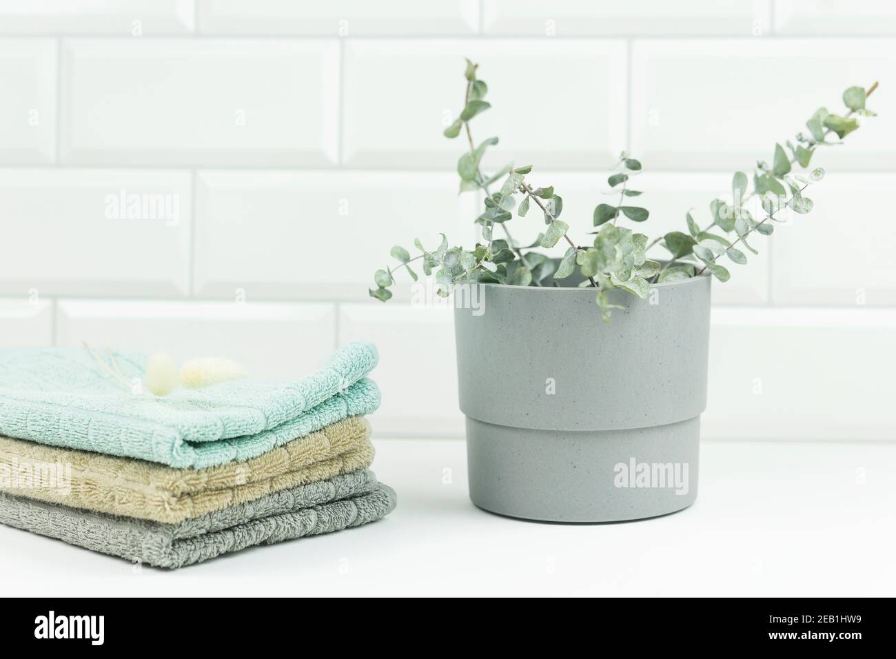 Baumwollhandtücher in neutralen Farben liegen auf einem Tisch in einem modernen Badezimmer. Daneben steht der Topf mit Eukalyptuszweigen Stockfoto