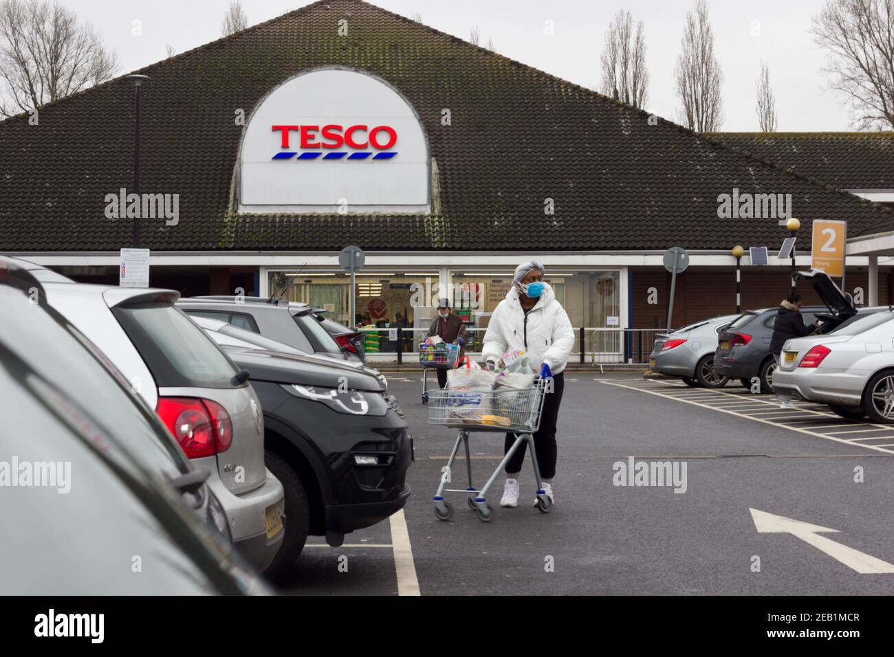 Frau Shopper trägt Gesichtsmaske schieben Shopping Trolley zu ihrem Auto in Tesco Supermarkt Parkplatz, Kent Stockfoto