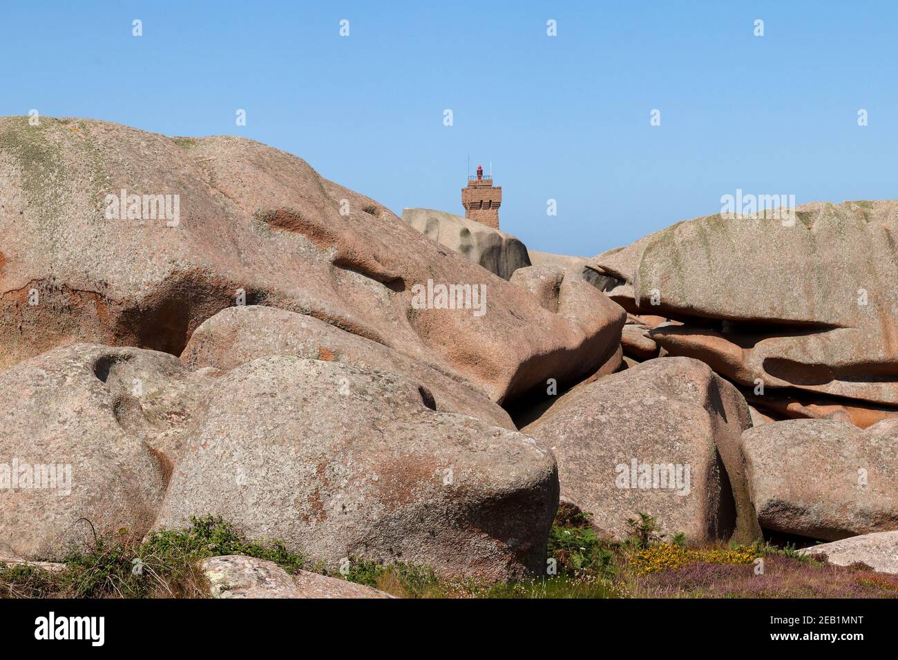 Felsbrocken an der Pink Granite Coast - Cote de Granit Rose - im Hintergrund die Spitze des Mittelwerts Ruz Lighthouse Stockfoto