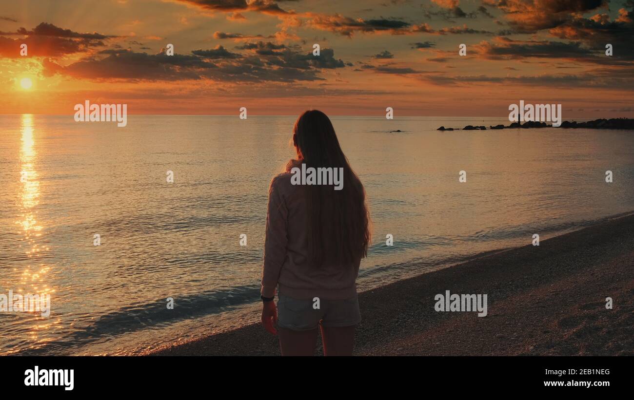 Frau mit ausgestreckten Armen genießen die Schönheit des Sonnenuntergangs auf dem Meer. Kranschuss. Stockfoto