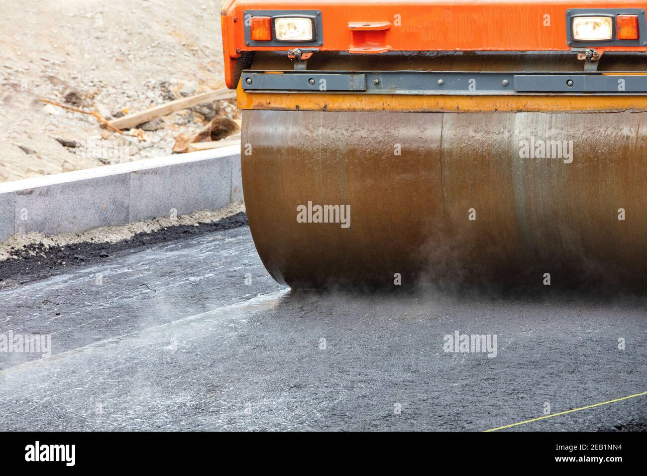 Der Metallzylinder der großen Vibrations-Straßenwalze verdichtet den frischen Asphalt und dämpft die heiße Oberfläche. Stockfoto