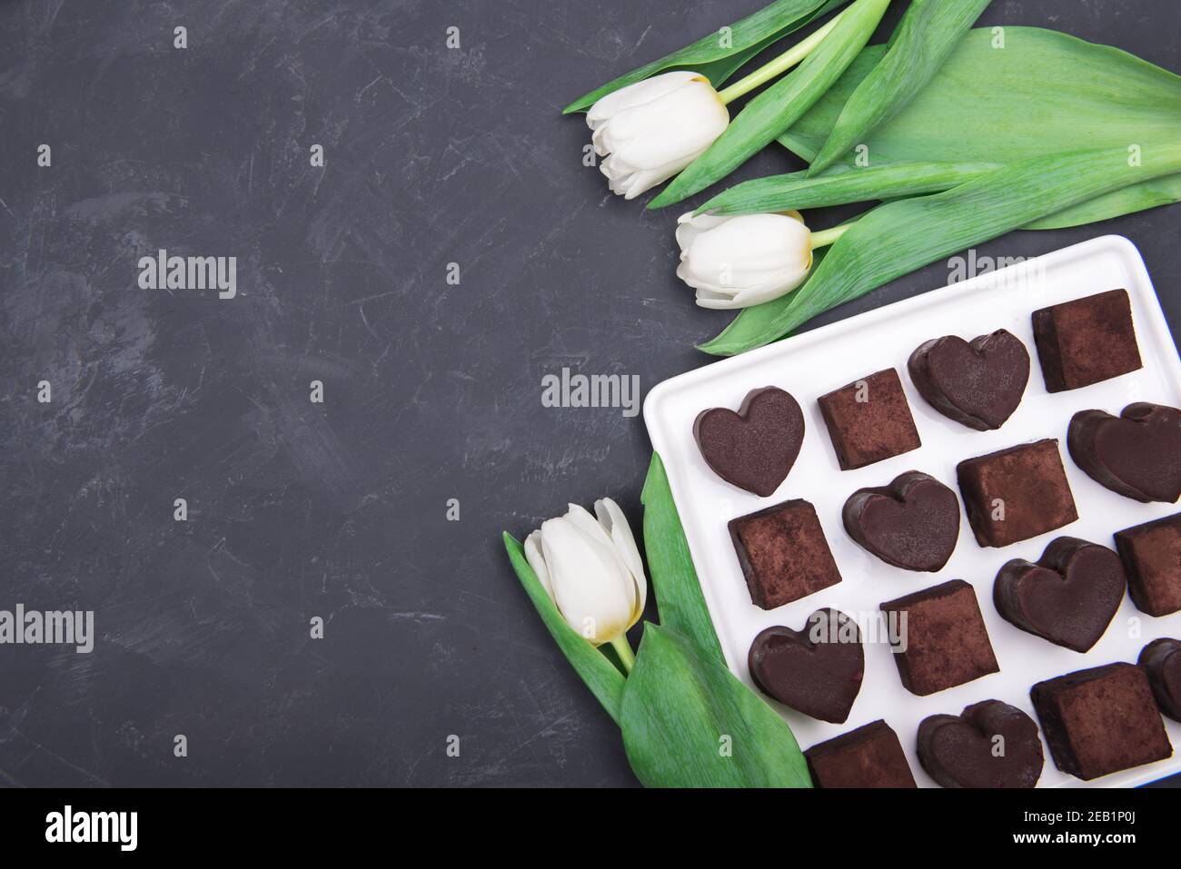 Geschenk-Box mit Schokolade Süßigkeiten Herzen und Tulpen auf dunklem Hintergrund. Wüste zum Valentinstag Stockfoto