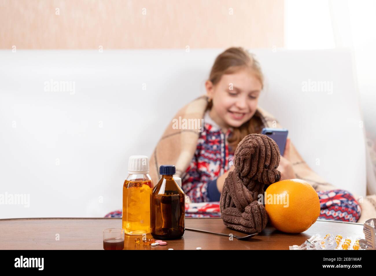 Eine Vielzahl von Medikamenten und Pillen. Ein krankes Kind hat Spaß am Telefon. Ein Kind mit einer Erkältung spielt auf dem Smartphone. Stockfoto