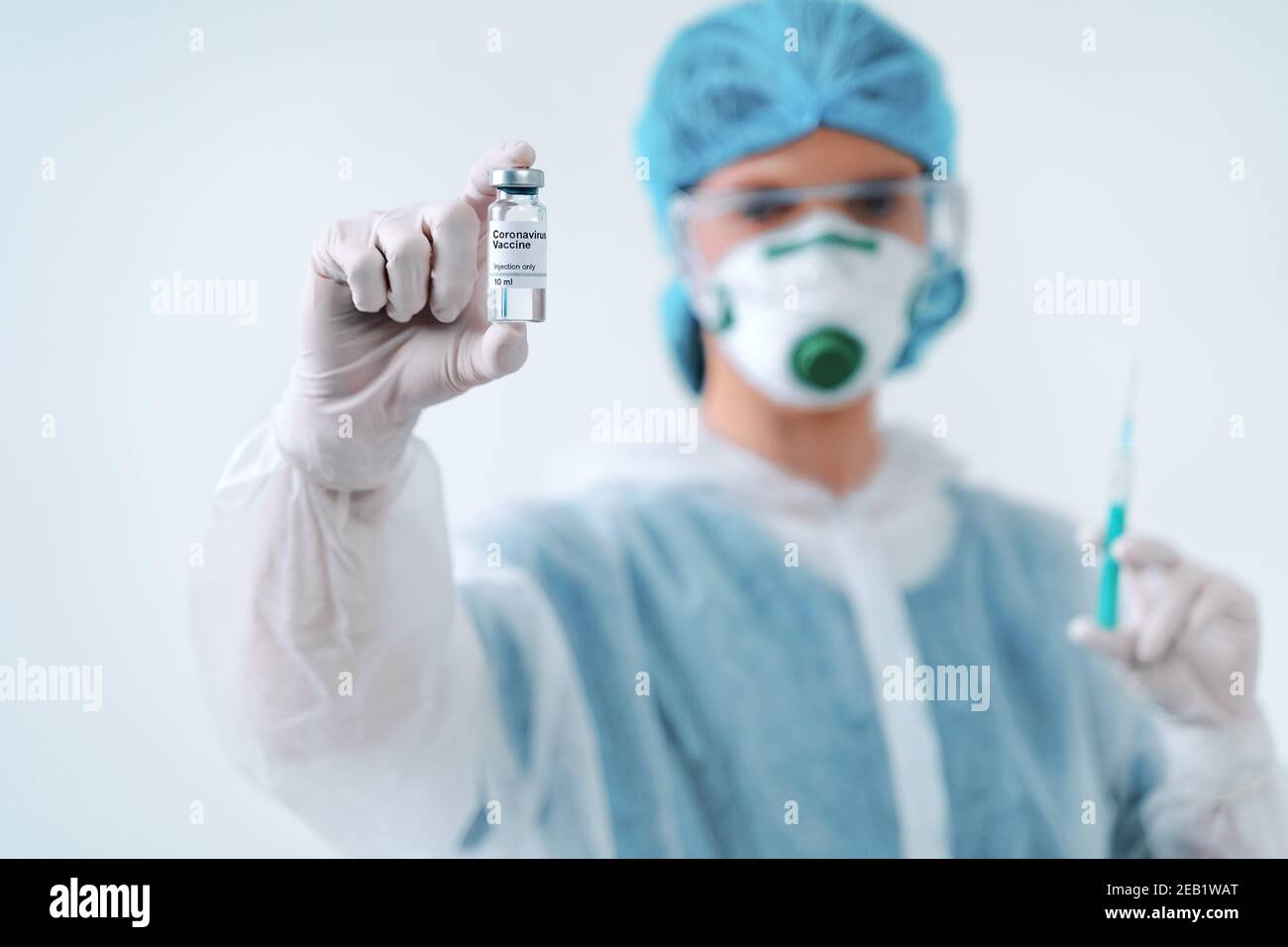 Krankenschwester in Schutzanzug und Maske hält eine Injektionsspritze und Impfstoff. Biologische Gefahr. Stockfoto