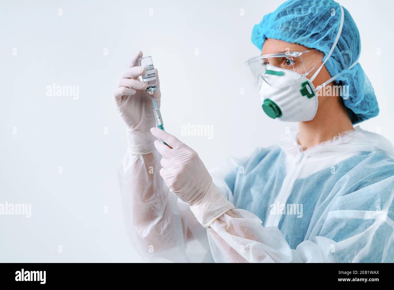 Krankenschwester in Schutzanzug und Maske hält eine Injektionsspritze und Impfstoff. Biologische Gefahr. Stockfoto