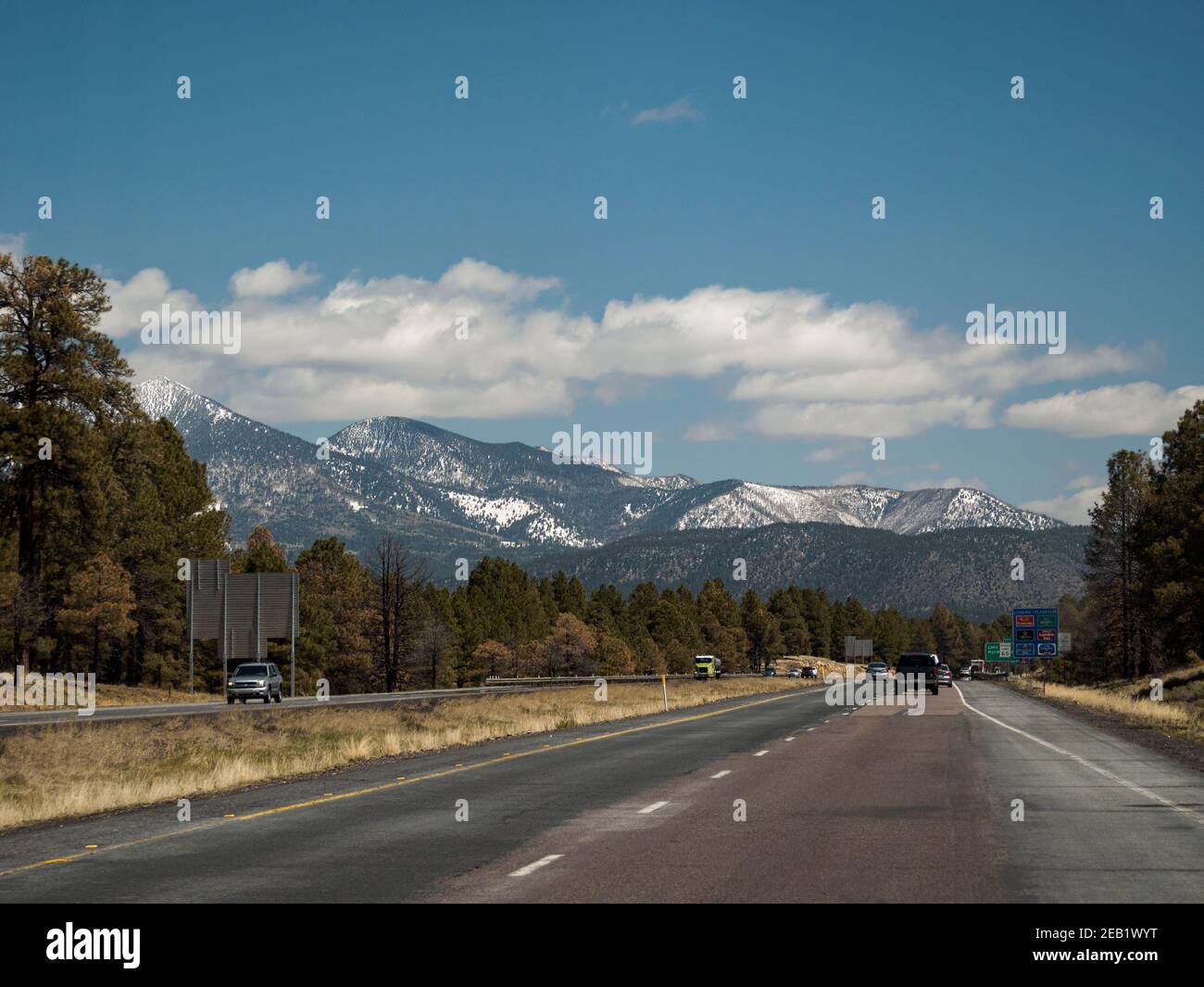 Roadtrip Fahrt auf dem Highway in der Nähe von Flagstaff, Arizona, mit blauem Himmel, Cumulus Wolken und schneebedeckten San Francisco Peaks, die Reste einer erodierten Straße Stockfoto