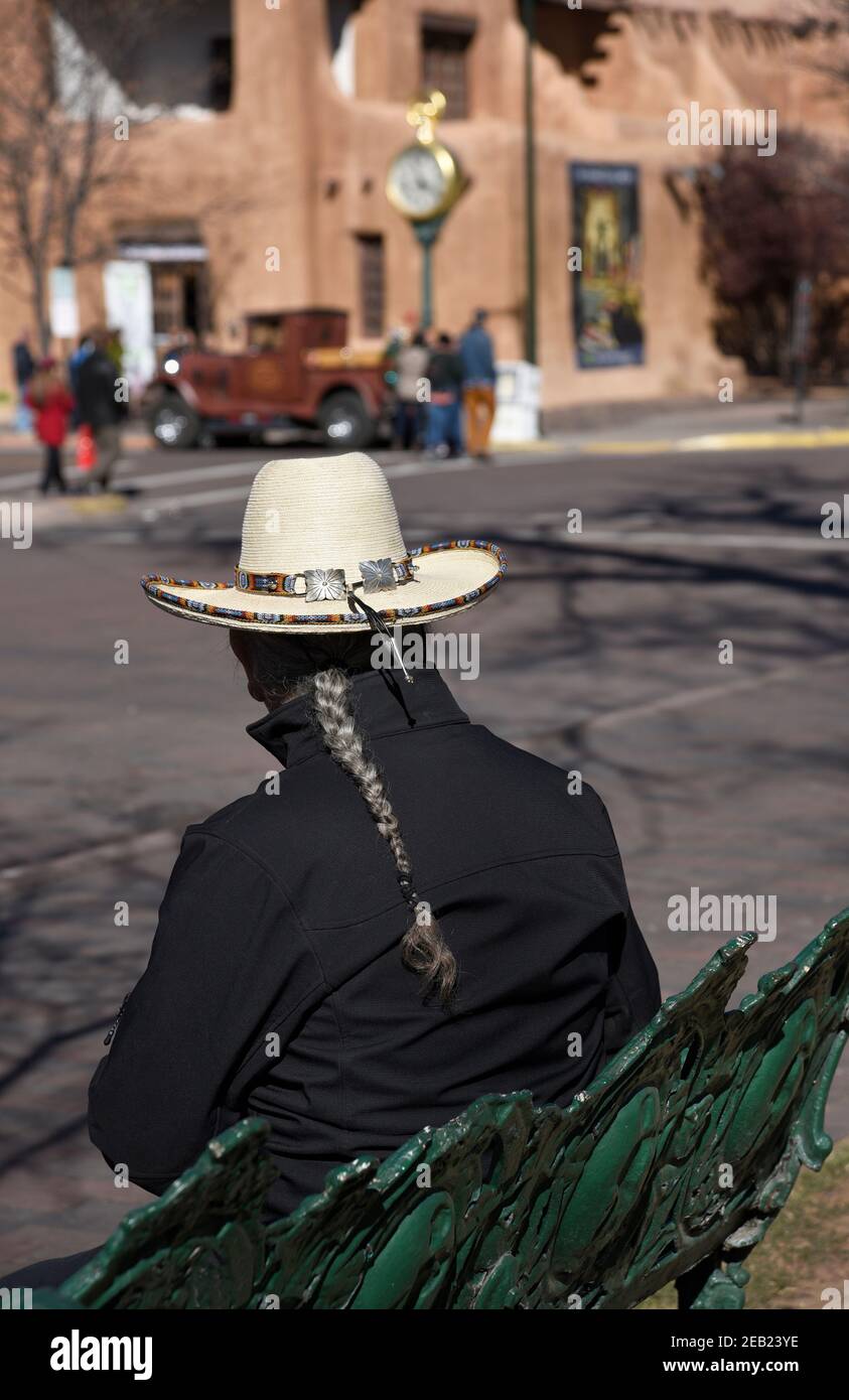 Ein hispanischer Mann mit geflochtenen Haaren (Ramon Jose Lopez, ein bekannter Künstler) sitzt auf einer Bank im historischen Plaza in Santa Fe, New Mexico. Stockfoto