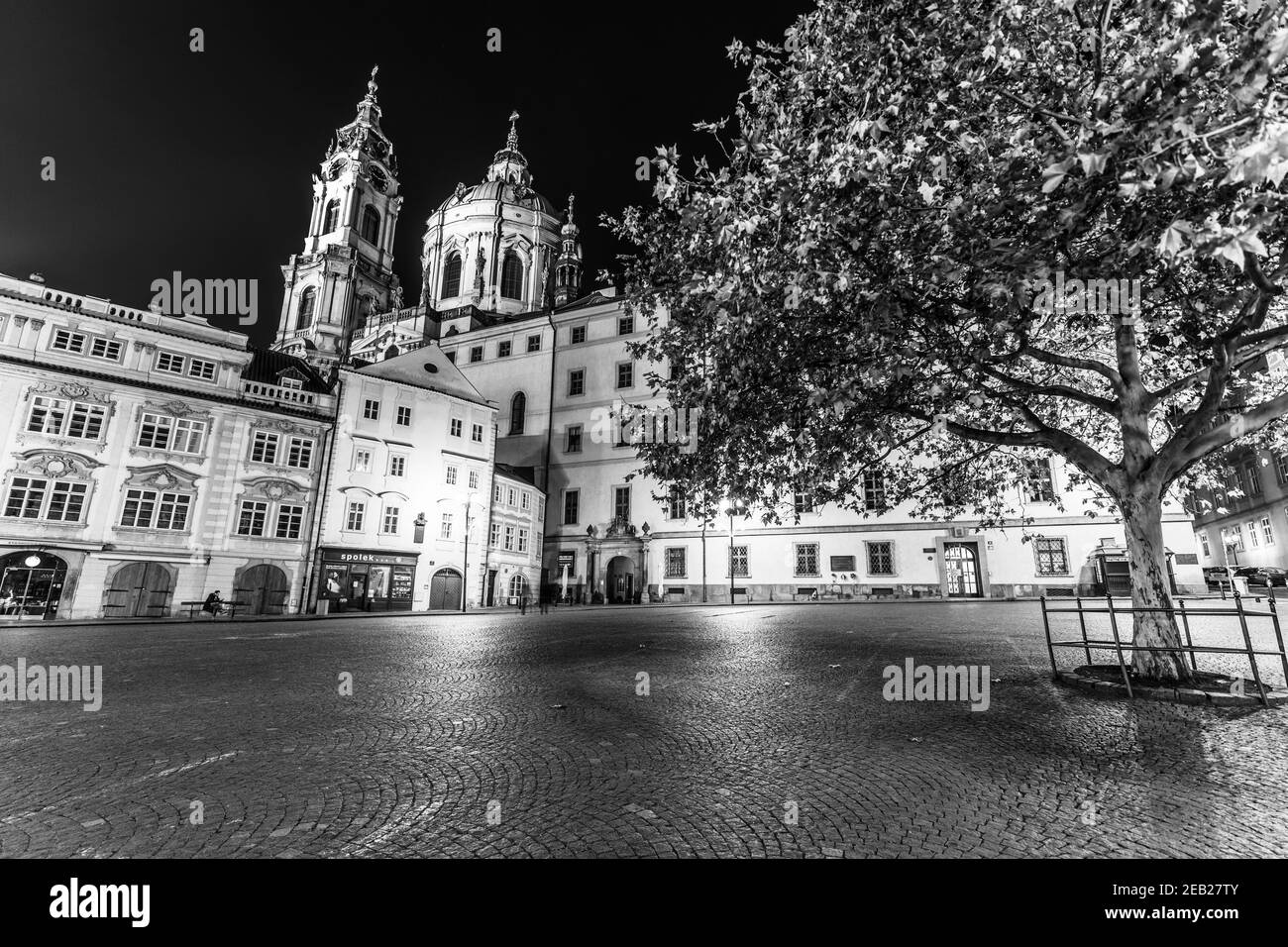 PRAG, TSCHECHISCHE REPUBLIK - 21. DEZEMBER 2020: Kleinstadt in Prag bei Nacht. Gepflasterte Straße und beleuchtete Gebäude mit barocker Kuppel des St. Nikolaus Stockfoto