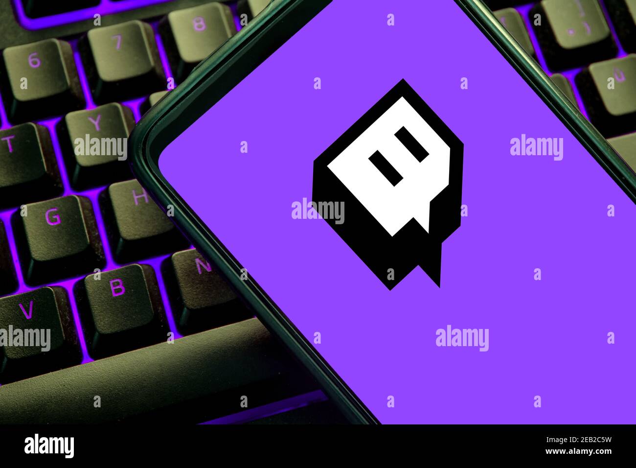 Twitch-Symbol auf einem Handybildschirm auf einer violett beleuchteten Gaming-Tastatur. Streaming-Website für Videospiele Stockfoto