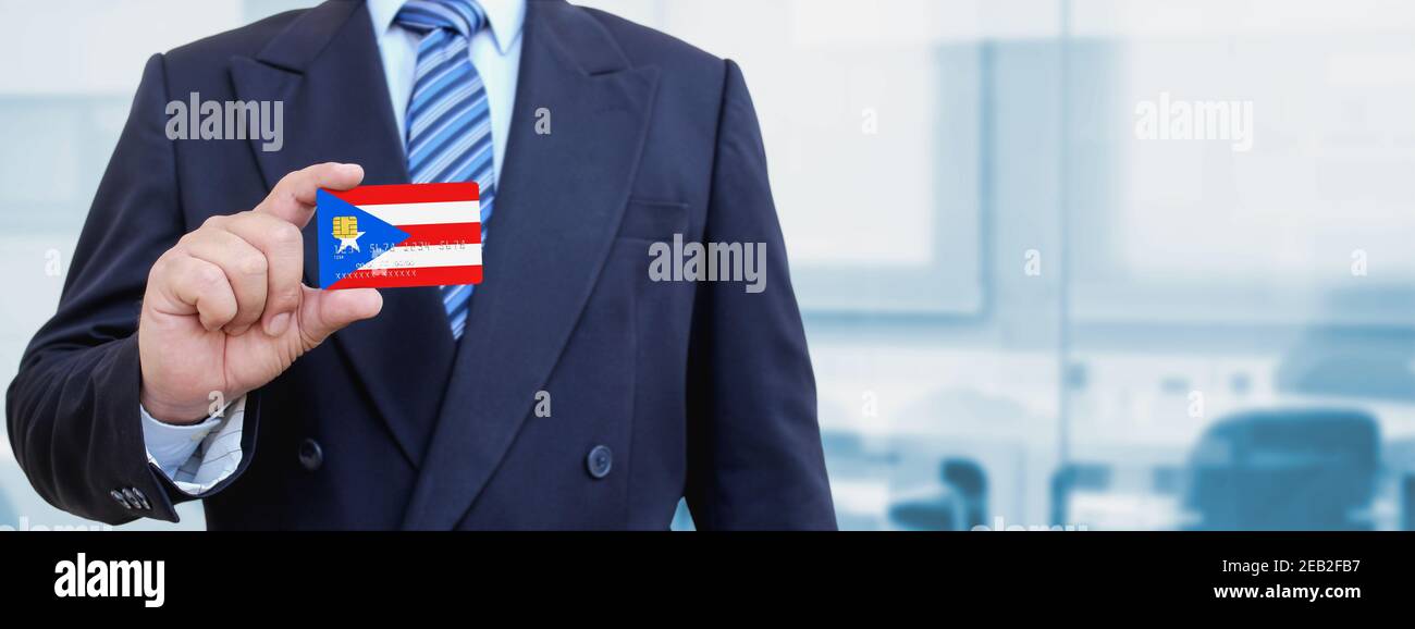 Zugeschnittenes Bild des Geschäftsmannes, der Plastikkreditkarte mit gedruckter Flagge von Puerto Rico hält. Hintergrund unscharf. Stockfoto