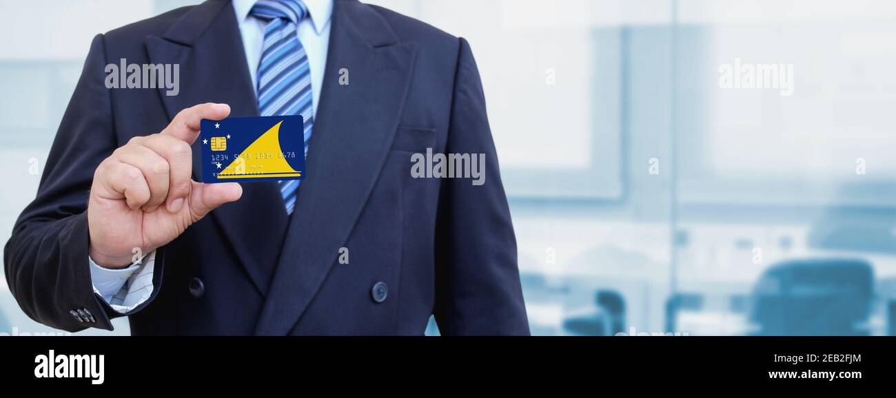 Zugeschnittenes Bild des Geschäftsmannes, der Plastikkreditkarte mit gedruckter Flagge von Tokelau hält. Hintergrund unscharf. Stockfoto