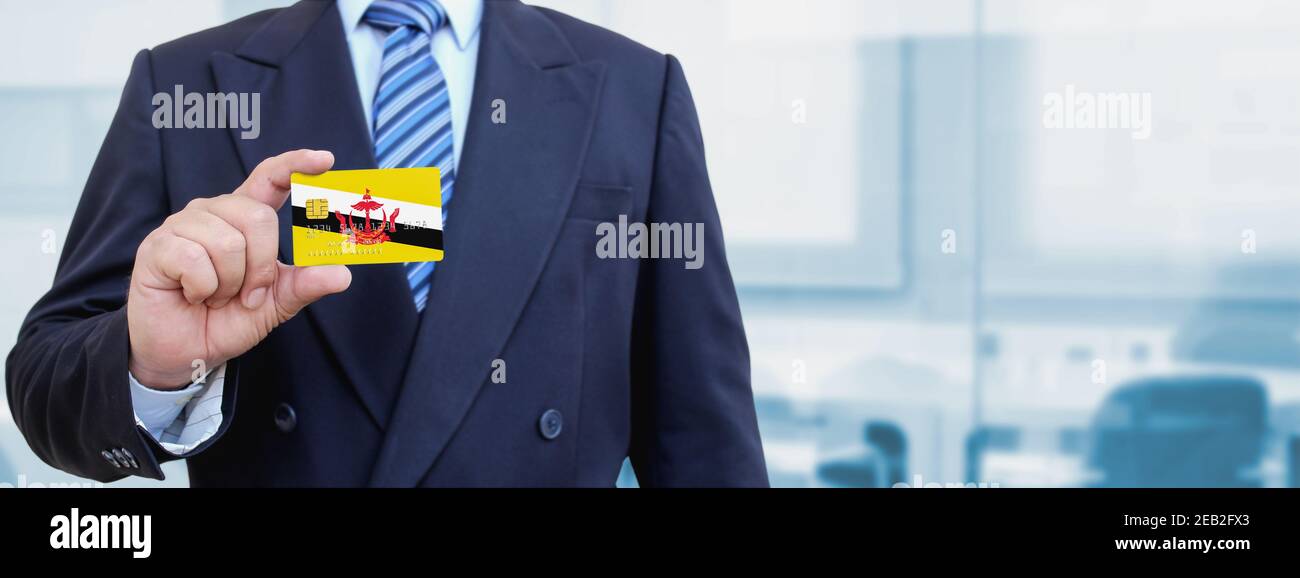 Zugeschnittenes Bild des Geschäftsmannes mit Plastikkreditkarte mit bedruckter Flagge von Brunei. Hintergrund unscharf. Stockfoto