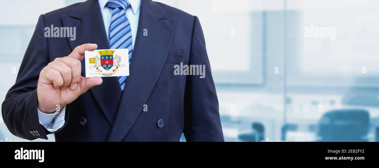 Zugeschnittenes Bild eines Geschäftsmannes, der eine Plastikkarte mit der bedruckten Flagge von Saint Barthelemy hält. Hintergrund unscharf. Stockfoto
