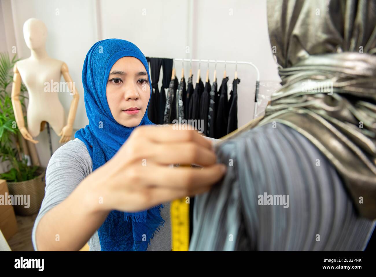 Asiatische muslimische Frau Designerin als Startup-Geschäft Inhaber arbeiten In ihrem Schneidergeschäft, das die Größe der Kleidung mit Klebeband misst Messen Stockfoto