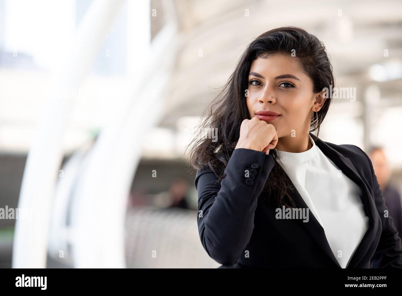 Schöne hispanische Geschäftsfrau mit Hand am Kinn am Gehweg im Freien In der Stadt Stockfoto