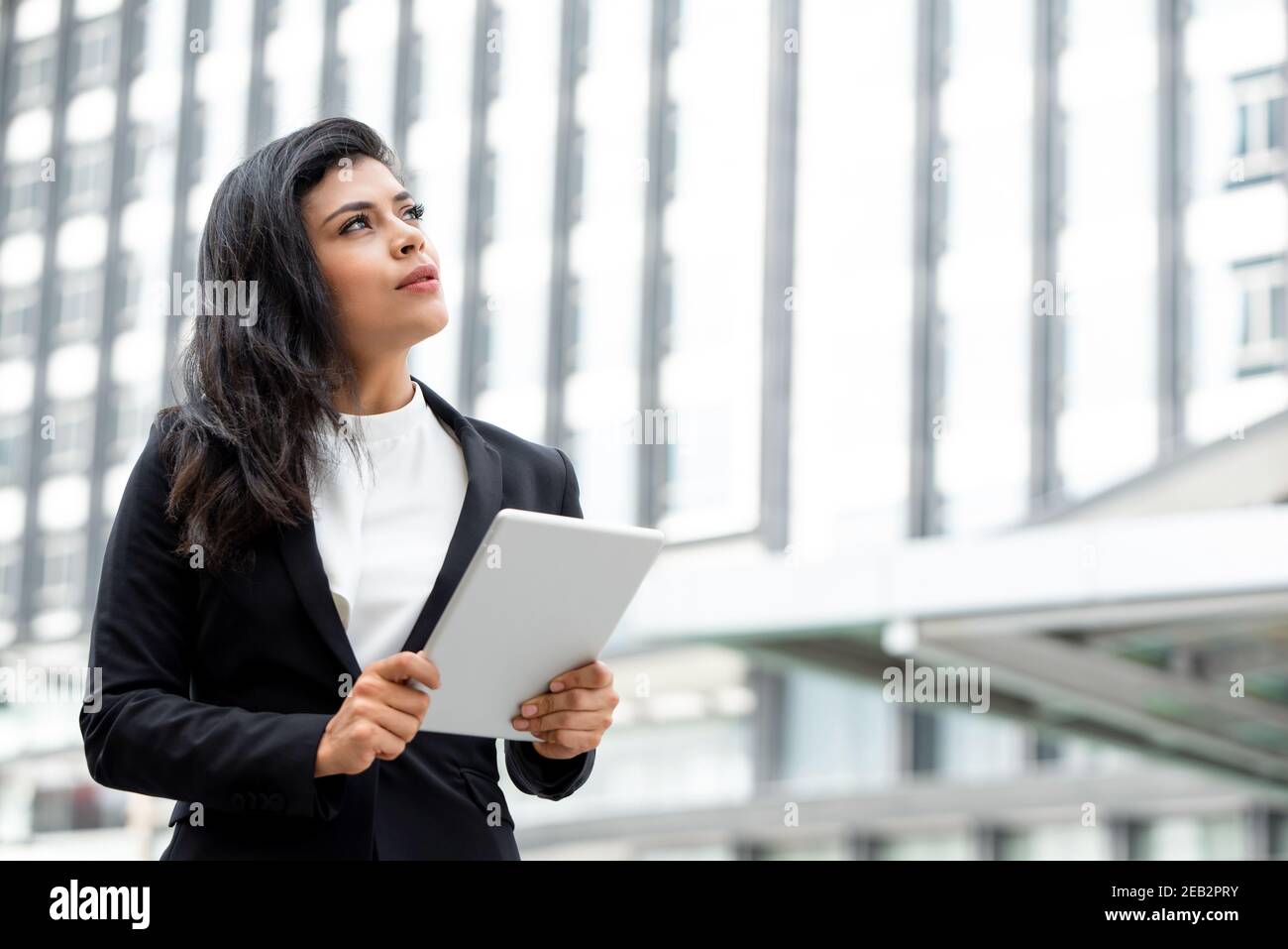 Junge schöne lateinische Geschäftsfrau hält Tablet-Computer und denken in Bürogebäude im Hintergrund Stockfoto