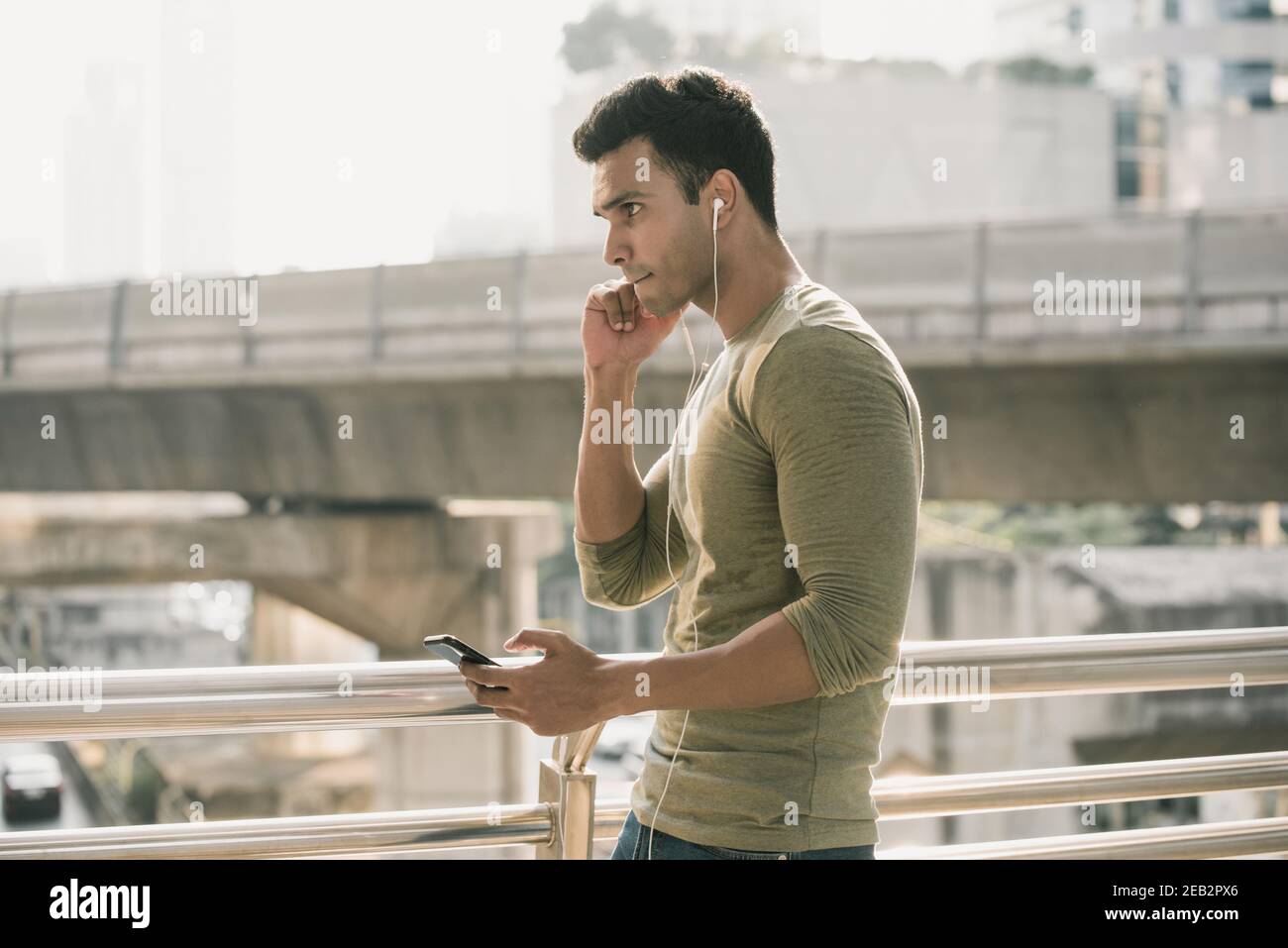 Junger hübscher indischer Mann, der Ohrhörer trägt und dabei Musik hört Zu Fuß in der Stadt Stockfoto