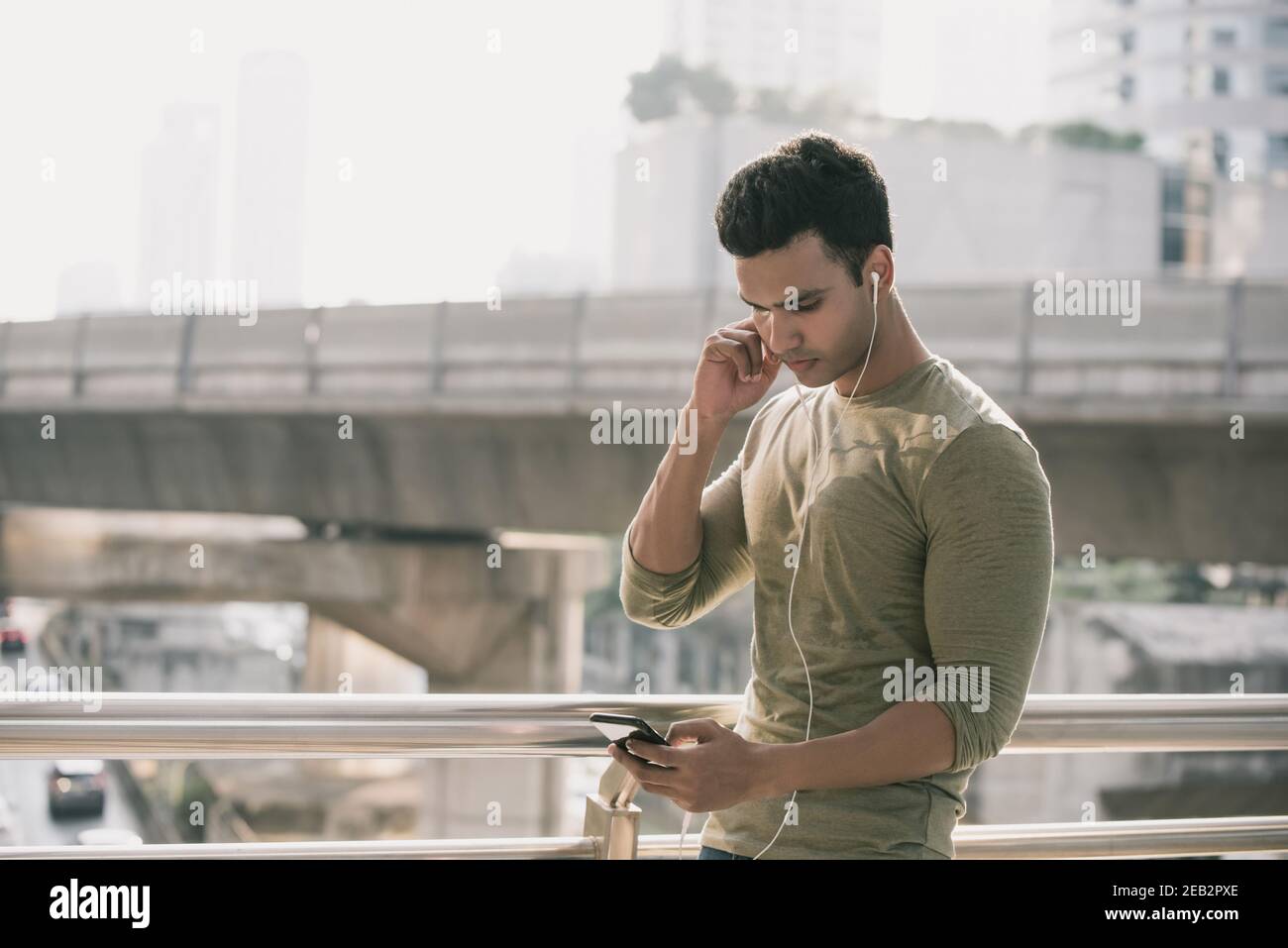 Junger hübscher indischer Mann, der Ohrhörer trägt und dabei Musik hört Zu Fuß in der Stadt Stockfoto