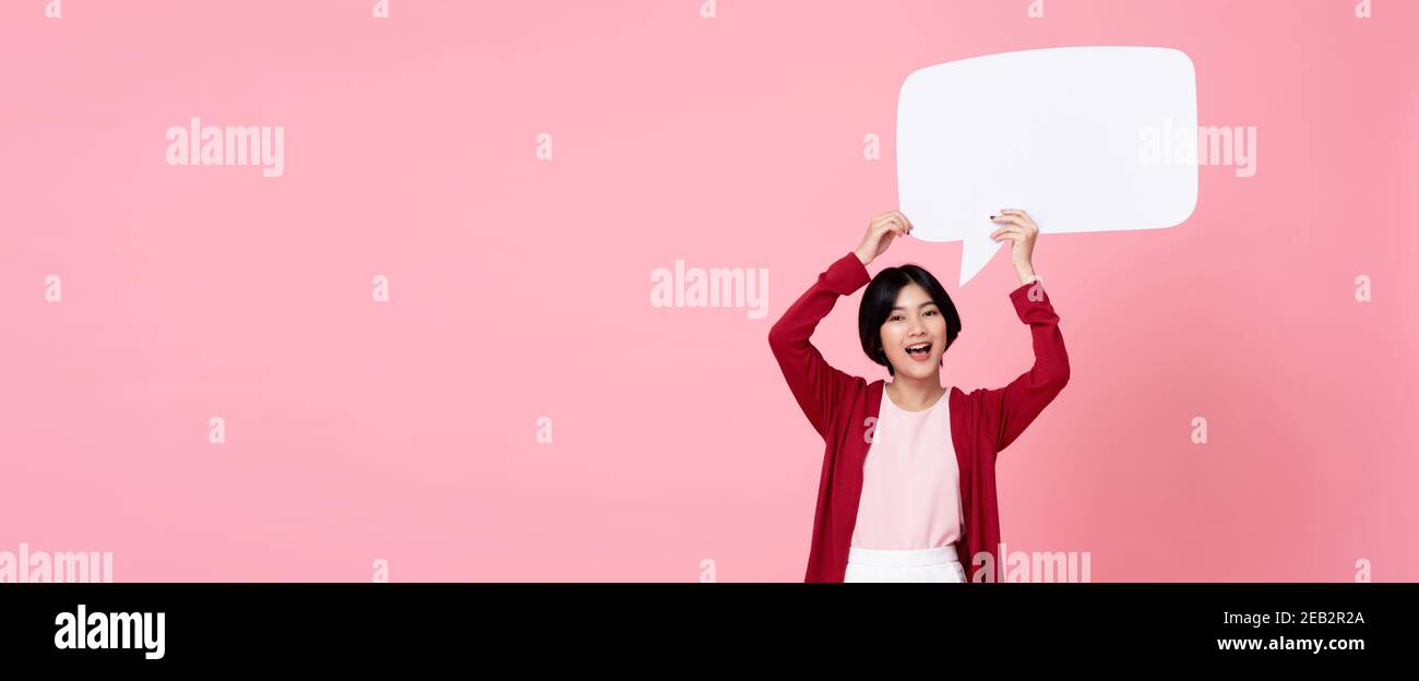 Lächelnde junge asiatische Frau hält leere Sprechblase in rosa Banner-Hintergrund mit Kopierbereich Stockfoto