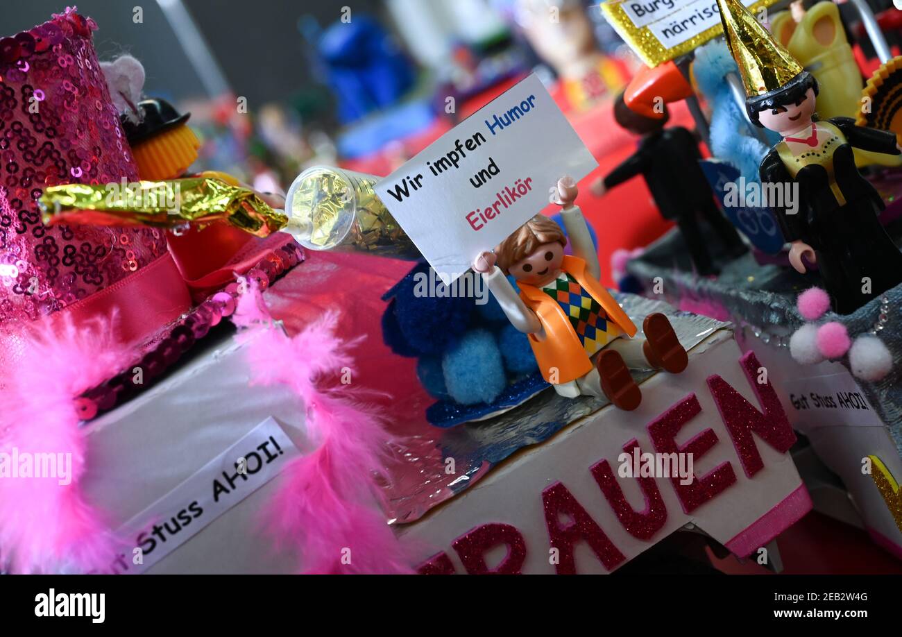 11. Februar 2021, Hessen, Offenbach/Main: Eine Playmobil-Figur, die einen Clown auf einem Miniaturwagen darstellt, hält ein Schild mit der Aufschrift: "Wir impfen Humor und Eiertau". Leidenschaftliche Bastler des Offenbacher Karnevalsvereins (OKV) haben wochenlang mühsam eine Miniaturversion der Parade nachgebaut, die im vergangenen Jahr durch Frankfurts Nachbarstadt rollte. Die Protagonisten wurden durch Spielzeugfiguren ersetzt. Dank eines umgebauten Grillmotors fahren sie am verkleideten Publikum und der ebenfalls nachgebildeten Kulisse vorbei. (Dpa 'Narren lachen und feiern dank kreativer Ideen trotz Corona PAN Stockfoto
