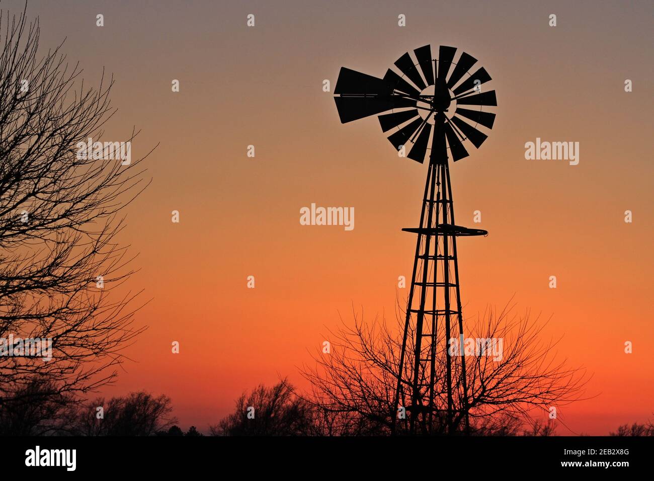 Kansas Windmill Silhouette mit Bäumen und einem bunten Himmel im Land nördlich von Hutchinson Kansas USA auf einer Weide. Stockfoto