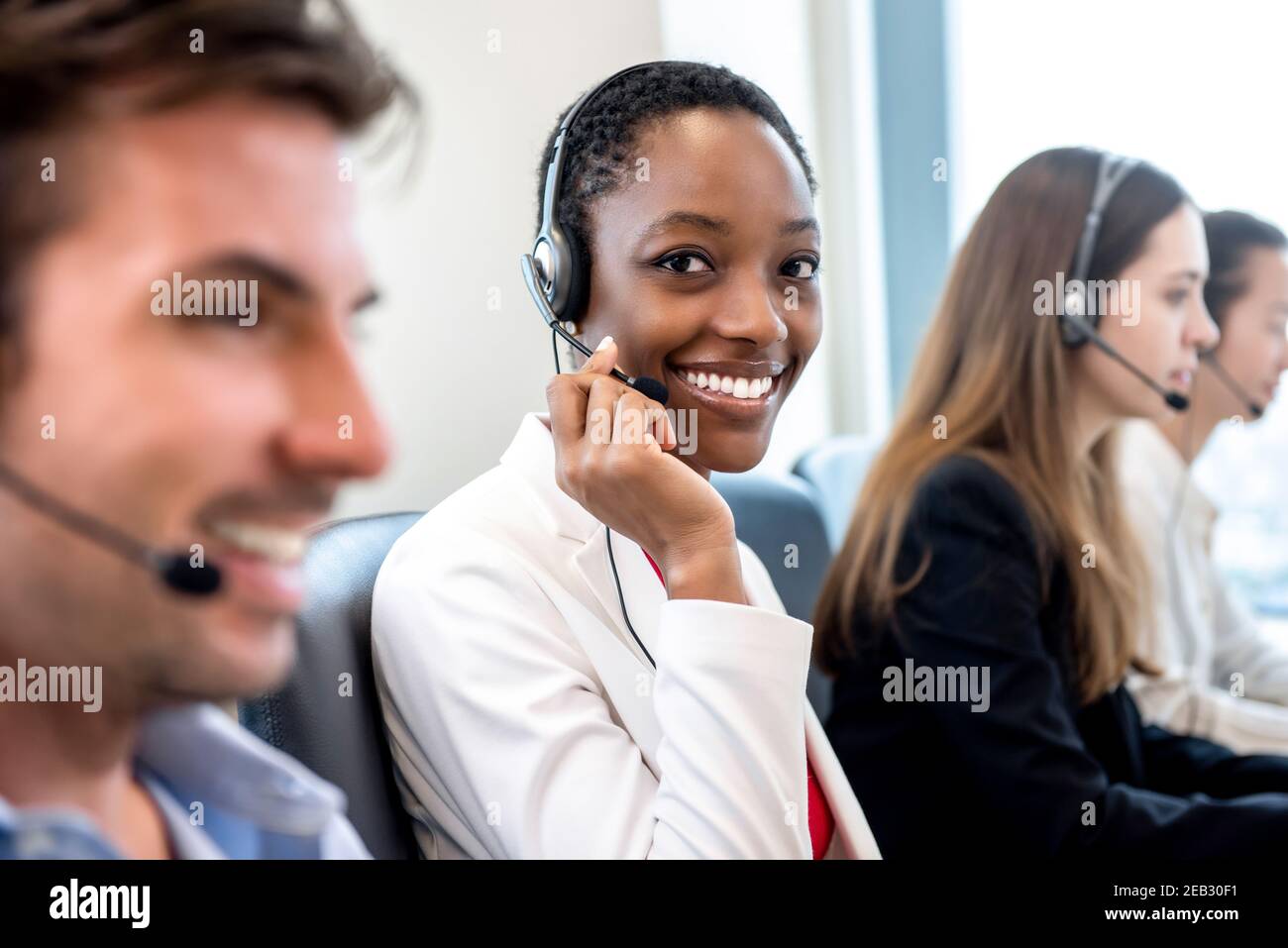 Lächelnd schöne afroamerikanische Frau, die im Callcenter-Büro arbeitet Mit einem vielfältigen Team als Kundendienstmitarbeiter Stockfoto