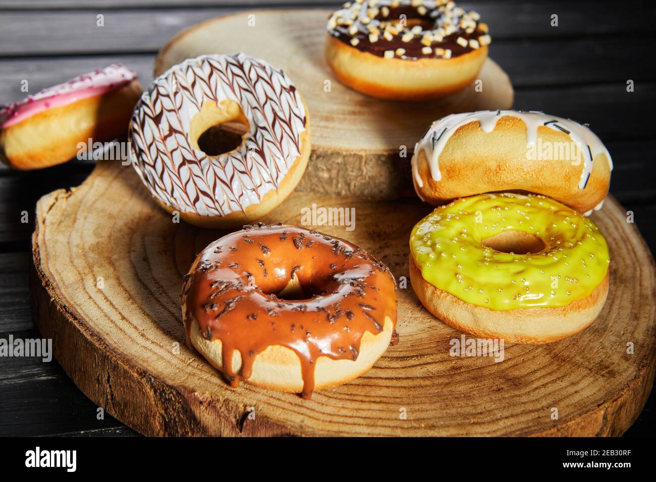 Bunte Donuts mit Glasur und Streuseln auf hölzernen Untersetzern auf schwarzem Hintergrund. Stockfoto