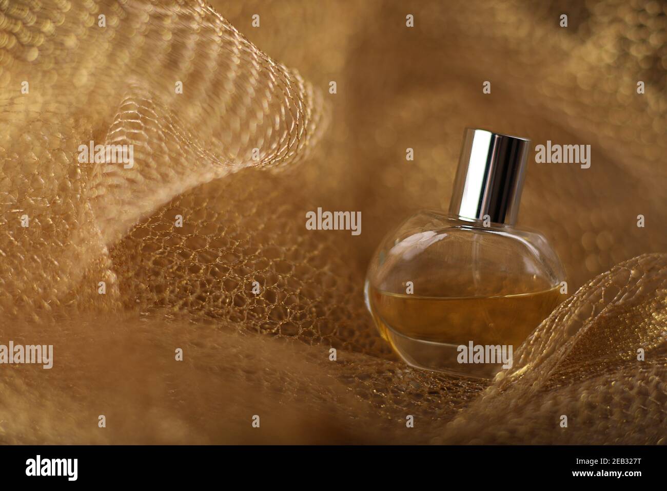 Flasche Glas von Parfüm auf Gold Stoff Mesh Hintergrund. Nahaufnahme im Studio mit Kopierbereich. Stockfoto