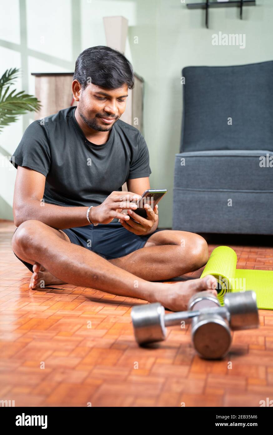 Junger Mann beschäftigt mit Handy während der Arbeit - Millennial Überprüfung Online-Übung Tutorials für das Training - Konzept der Heimfitnessraum wegen Coronavirus Stockfoto