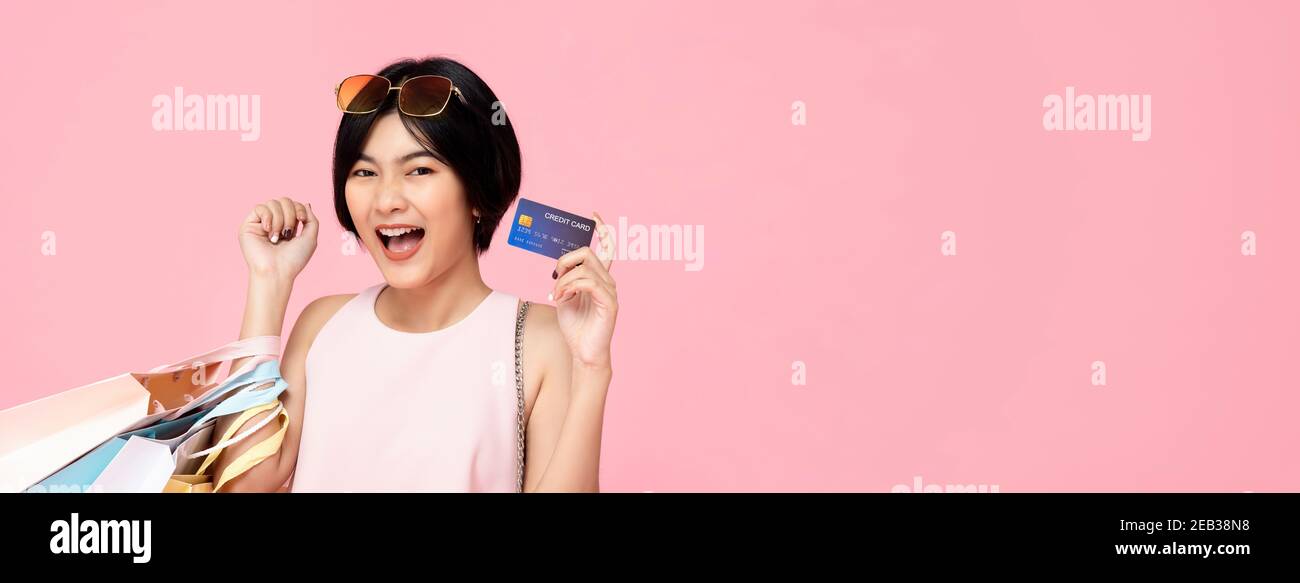 Junge hübsche asiatische Frau mit Einkaufstaschen mit Kreditkarte In der Hand Studio erschossen isoliert auf rosa Banner Hintergrund mit Speicherplatz kopieren Stockfoto