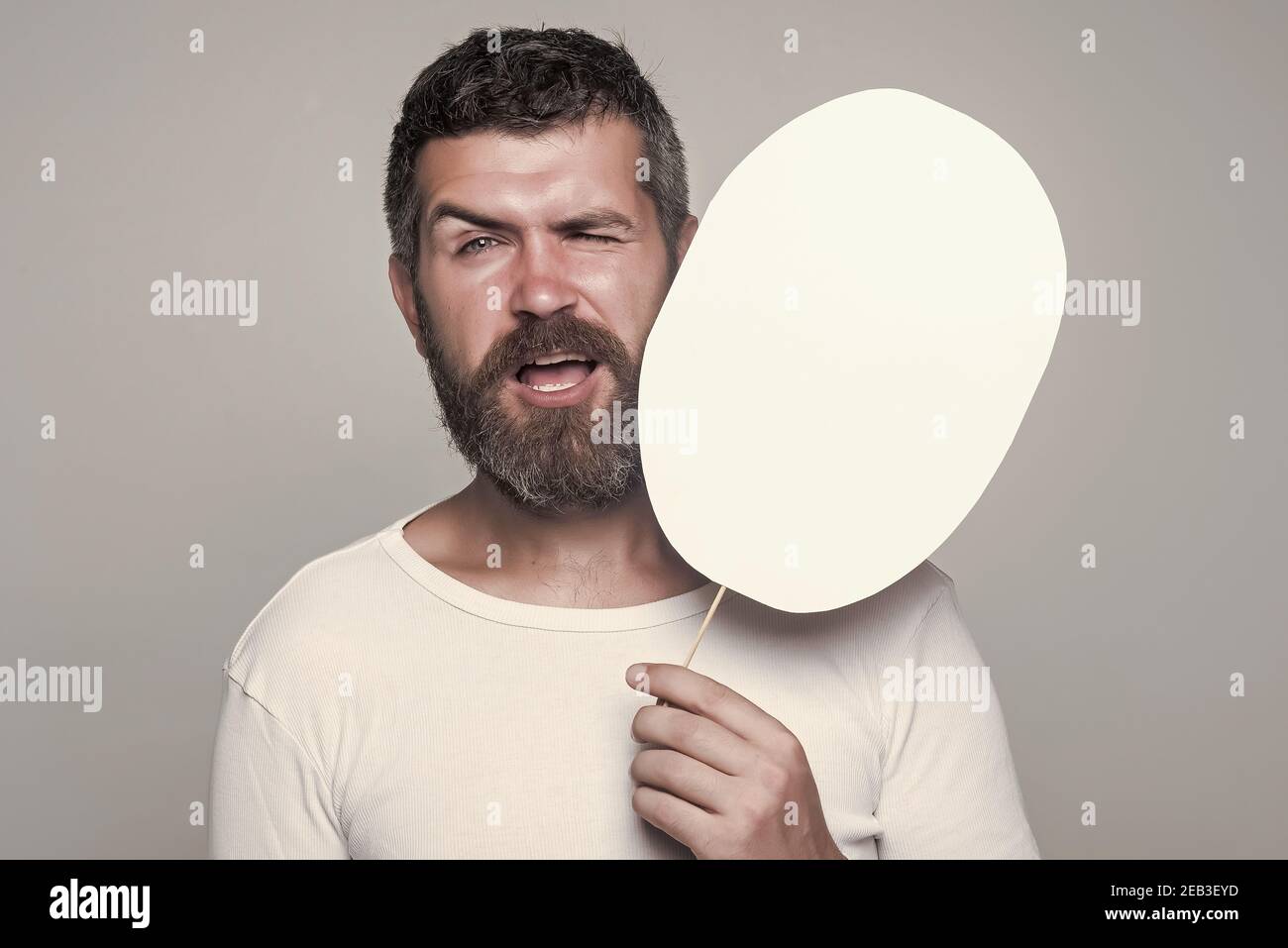 Hipster mit winkenden Gesicht halten Papier Namensschild. Mann auf grauem Hintergrund, Kopierraum. Gefühl und Emotionen. Stockfoto
