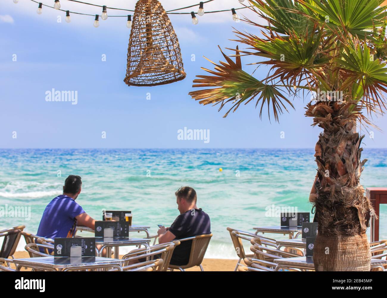 Barcelona, Spanien, August 2019. Zwei Männer sitzen im Restaurant mit Meerblick im Sommer, entspannen auf einer Café-Terrasse. Umweltfreundliches Design mit Weidenlam Stockfoto