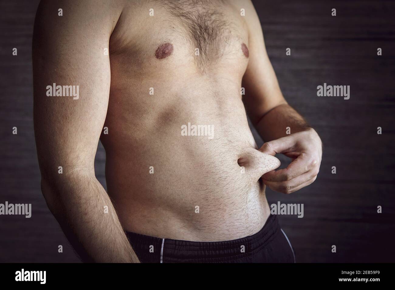 Ein erwachsener Mann quetscht eine Fettschicht auf seinen Bauch. Ein Mann mit einer guten Figur quetscht die Haut auf seinen Bauch. Stockfoto