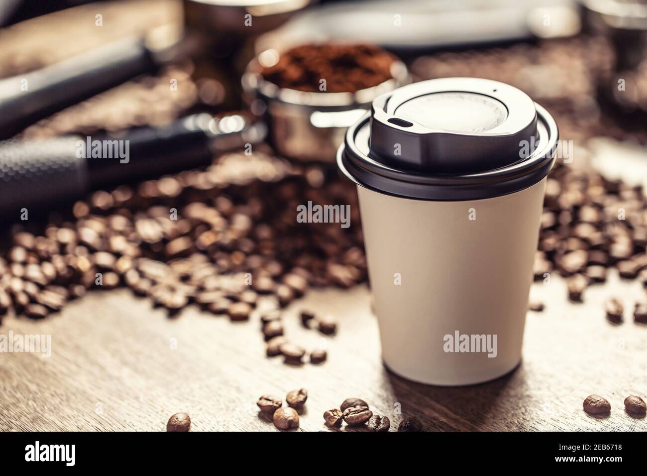 Papiertasse mit Kunststoffdeckel und Kaffee mit Kaffeebohnen und gemahlenem Kaffee im Hintergrund. Stockfoto