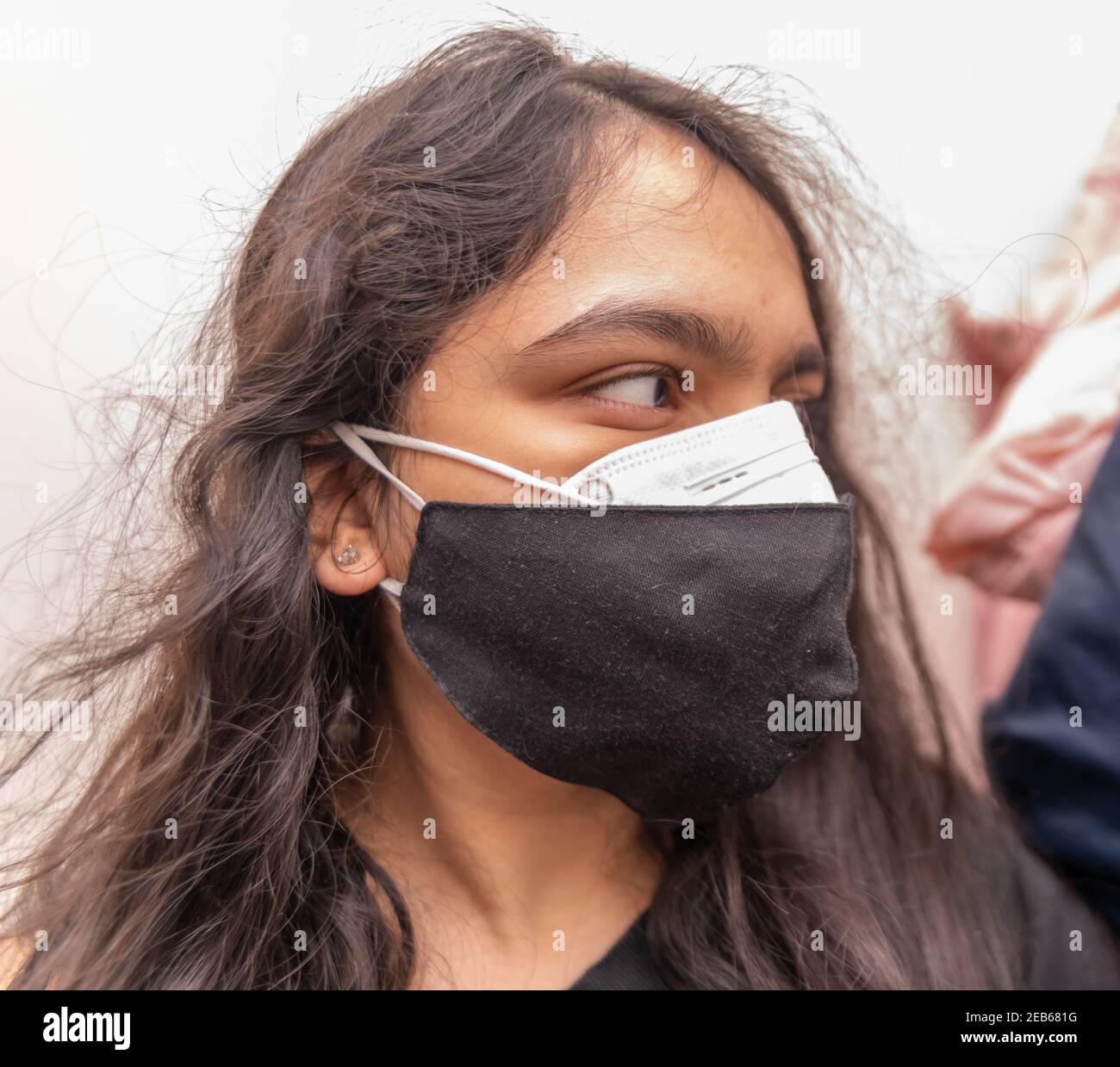 Indische Frau trägt zwei Gesichtsmasken, eine N95 und eine Stoffmaske für covid-19 Prävention. Seitenansicht. Doppelmaskierung wird von der US-amerikanischen CDC vorgeschlagen. Stockfoto
