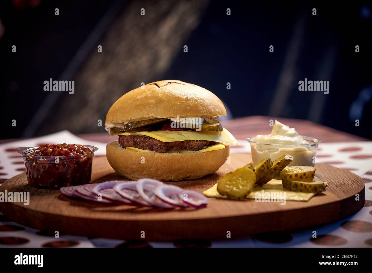 Cheeseburger und Zutaten auf einem Holzbrett auf dunklem Hintergrund. Stockfoto