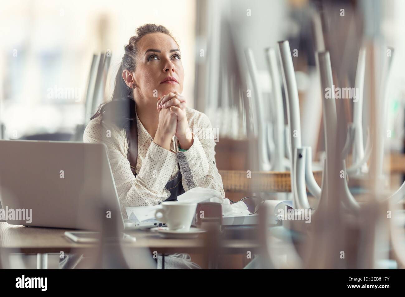 Geschäftsbesitzerin betet in einem geschlossenen Restaurant für bessere Zeiten und das Ende der Coronavirus-Pandemie. Stockfoto