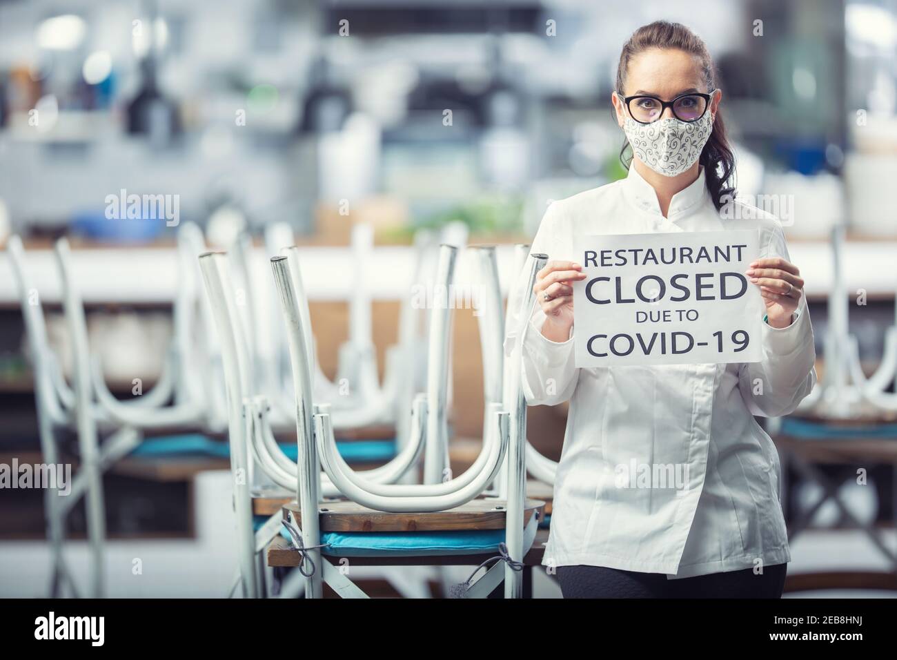 Die Köchin trägt eine Gesichtsmaske und hält ein Schild für das Restaurant, das wegen Covid-19 geschlossen ist. Stockfoto