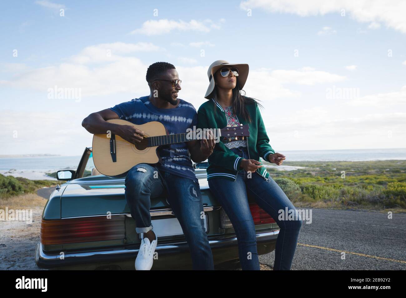 Diverse Paare, die am sonnigen Tag neben Cabrio eine Pause am Straßenrand machen Auto der Mann, der Gitarre spielt Stockfoto