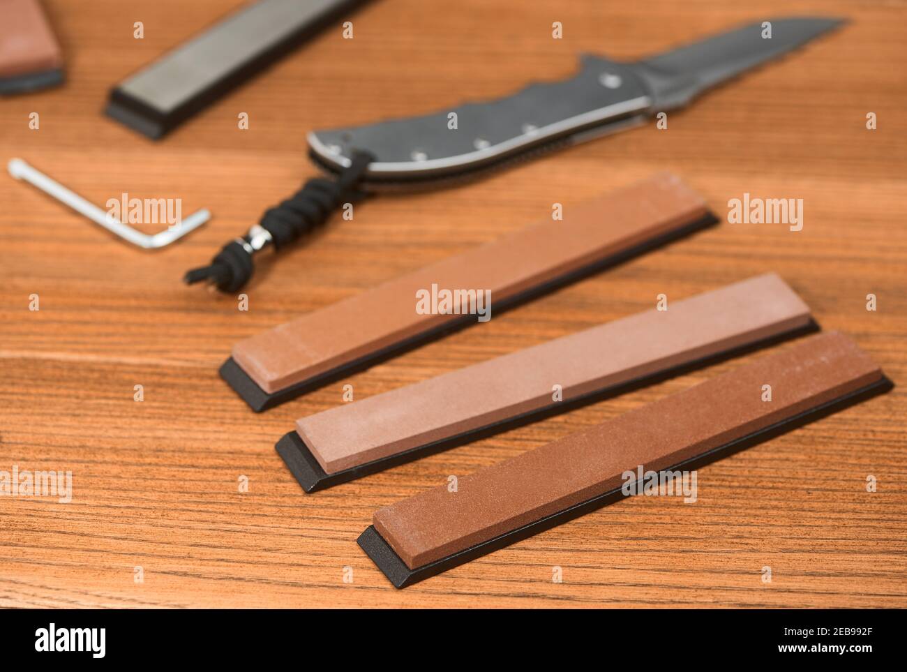 Verschiedene Wetzsteine, ein Klappmesser und ein Sechskantschlüssel auf Holzhintergrund Stockfoto