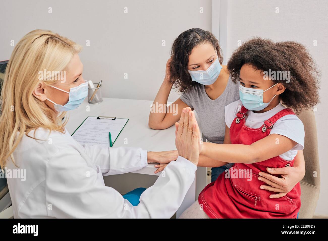 Afroamerikanisches Kind mit ihrer Mutter, die bei der Hausarztkonsultation Schutzmasken trägt. Globale Pandemie Stockfoto