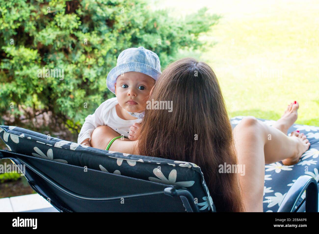 Kind in den Armen der Mutter, neue Mutter ruht mit einem 5 Monate alten Baby auf einem Liegestuhl Stockfoto
