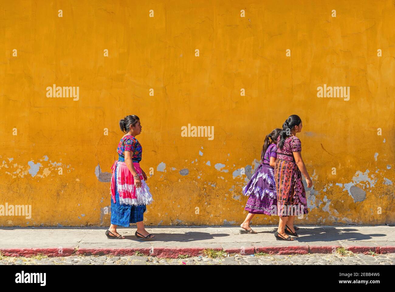 Guatemaltekische maya-indigene Frauen, die an einer Kolonialfassade vorbeilaufen, Antigua, Guatemala. Stockfoto Guatemaltekische maya-indigene Frauen, die an einer Kolonialfassade vorbeilaufen, Antigua, Guatemala. Stockfoto
