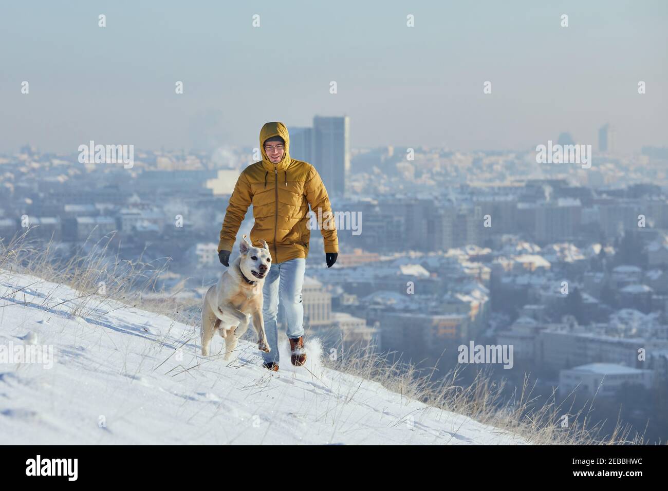 Glücklicher junger Mann mit Hund im Winter. Haustierbesitzer mit seinem labrador Retriever im Schnee gegen die Stadt. Prag, Tschechische Republik Stockfoto