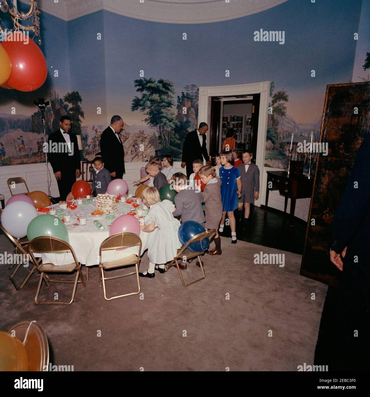 Geburtstagsfeier für Caroline Kennedy und John F. Kennedy, Jr.. Kleine Kinder kommen im Presidentu2019s Dining Room (Residenz) des Weißen Hauses, Washington, D.C. zu einer gemeinsamen Geburtstagsfeier für Caroline Kennedy und John F. Kennedy, Jr.; First Lady Jacqueline Kennedy steht in der Nähe der Tür im Hintergrund. Caroline (Mitte links, meist versteckt) geht zum Tisch links; Avery Hatcher, Sohn von Associate Press Secretary, Andrew T. Hatcher, geht links von Caroline; Maria Shriver geht in der Mitte rechts. Ebenfalls im Bild: White House Mau00eetre du2019Hotel, Charles E. Ficklin; White House Butlers, Jo Stockfoto