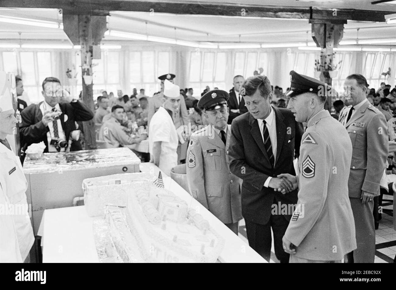 Europareise: Deutschland, Hanau: Präsident Kennedy hat in der Fliegerhorst Kaserne um 12:15pm Uhr mit US-Truppen und ihren Offizieren zu Mittag gegessen. Präsident John F. Kennedy schüttelt die Hände mit einem nicht identifizierten US-Armeefeldwebel, als er einen Kuchen in Form von PT-109 in der Messehalle der Fliegerhorst Kaserne in Hanau (Bundesrepublik) betrachtet. Militärhilfe für Präsident Kennedy, General Chester V. Clifton, steht ganz rechts. Ebenfalls im Bild: Associated Press Fotograf, Henry Burroughs; White House Secret Service Agent, Frank Yeager. Stockfoto