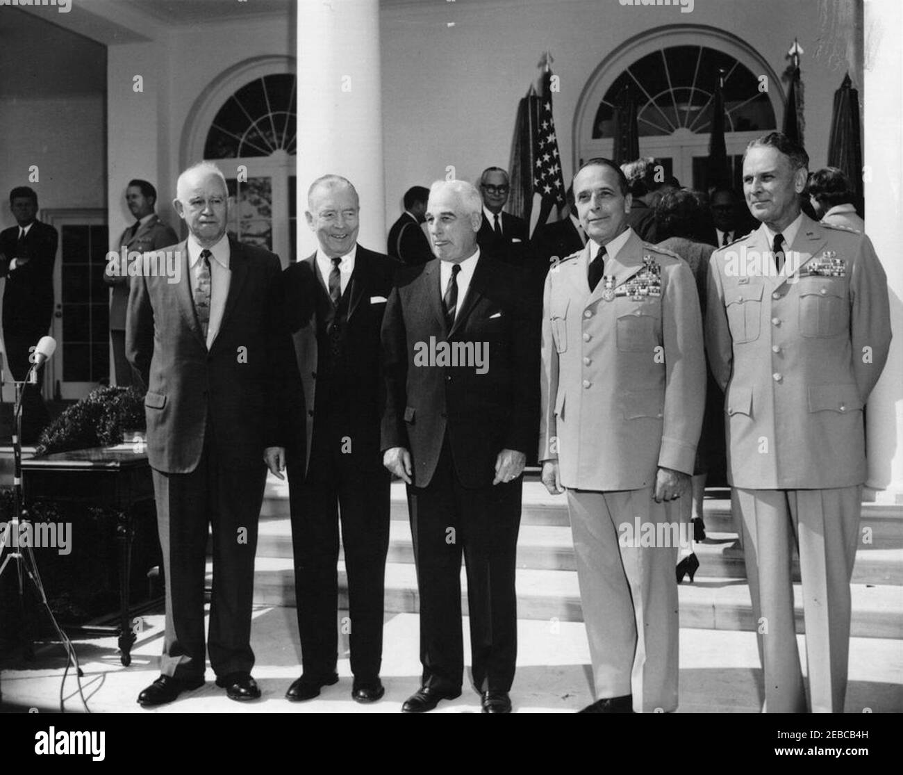 Vereidigung, General Maxwell Taylor, Chairman, JCS, 12:00pm Uhr. Der neu ernannte Vorsitzende der Joint Chiefs of Staff (JCS), General Maxwell D. Taylor, steht während seiner Vereidigung mit den ehemaligen Vorsitzenden der JCS zusammen. Von links nach rechts (im Vordergrund): General Omar Bradley; Admiral Arthur W. Radford; General Nathan F. Twining; General Lyman L. Lemnitzer; General Taylor. Präsident John F. Kennedy (hinten links, mit gefalteten Armen) und Militärhilfe an den Präsidenten, General Chester V. Clifton, stehen in der West Wing Colonnade. Ebenfalls im Bild: Naval Aide to the President, Captain Tazewell T. Shep Stockfoto