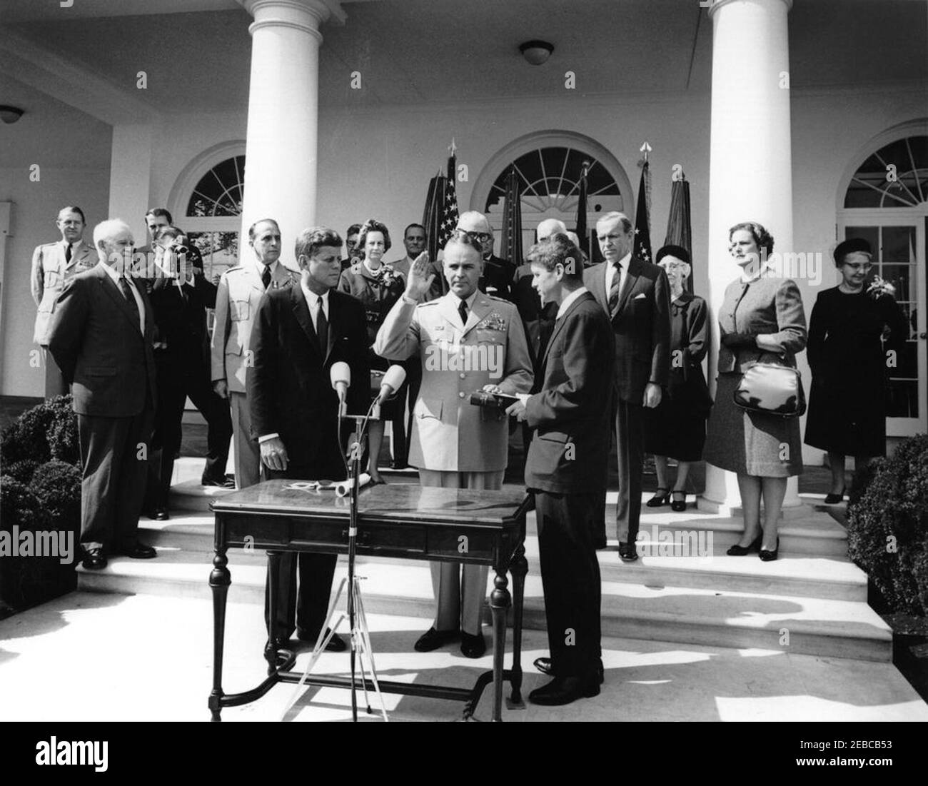 Vereidigung, General Maxwell Taylor, Chairman, JCS, 12:00pm Uhr. Präsident John F. Kennedy (Mitte links) und andere beobachten als General Maxwell D. Taylor (mit rechter Hand angehoben und linke Hand auf der Bibel) wird als Vorsitzender der Joint Chiefs of Staff (JCS) vereidigt; Generalstaatsanwalt Robert F. Kennedy (Mitte rechts, hält Bibel), verwaltet den Amtseid. Von den Stufen der West Wing Colonnade, ganz hinten beginnend (von links nach rechts): Military Aide an den Präsidenten, General Chester V. Clifton; General Omar Bradley; Naval Aide an den Präsidenten, Captain Tazewell T. Shepard, Stockfoto