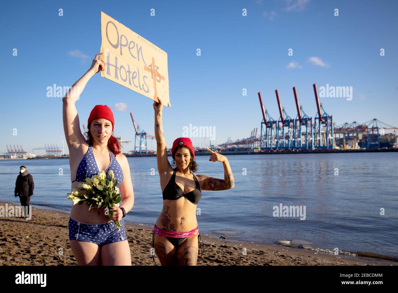 Hamburg, Deutschland. Februar 2021, 12th. Eve Champagne (l.), Burlesque-Künstlerin, und Natalie Warncke halten ein Schild mit der Aufschrift "Offene Hotels" und 13 weiße Rosen, bevor sie mit anderen Eisbathern in der eiskalten Elbe bei Övelgönne schwimmen gehen. Mehrere Dutzend mutige Menschen stürzten sich am Freitag für einen guten Zweck in die drei Grad kalte Elbe. Die wöchentliche Aktion der "Eisbather" soll Spenden für Obdachlose fördern. Quelle: Christian Charisius/dpa/Alamy Live News Stockfoto