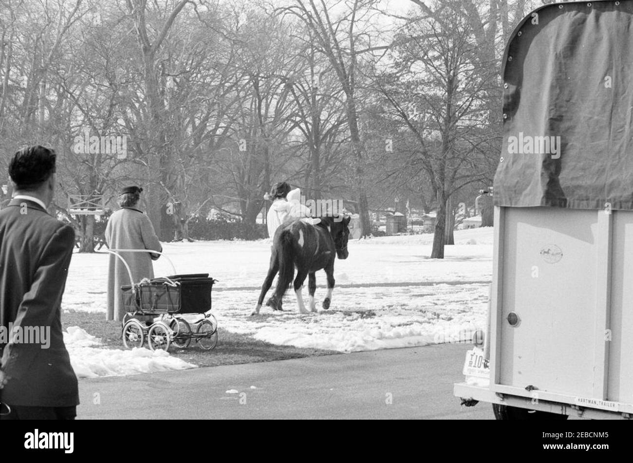 First Lady Jacqueline Kennedyu0027s (JBK) Schlittenfahrt auf dem South Lawn. First Lady Jacqueline Kennedy hält ihren Sohn John F. Kennedy, Jr. auf Caroline Kennedyu0027s Pony Macaroni auf dem schneebedeckten South Lawn. Nicht identifizierter Mann und Nanny der Kennedy-Kinder, Maud Shaw (mit Kinderwagen), Blick auf von links. White House, Washington, D.C. Stockfoto